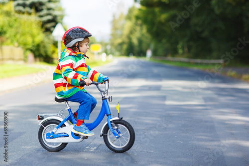 Adorable kid boy in red helmet and colorful raincoat riding his © Irina Schmidt