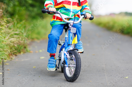 Child in colorful raincoat riding his first bike