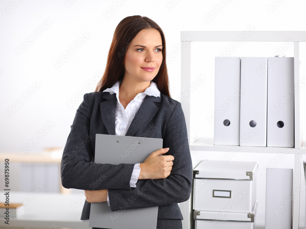 Attractive young businesswoman standing near desk with folder in Attractive young businesswoman standing near desk with folder in