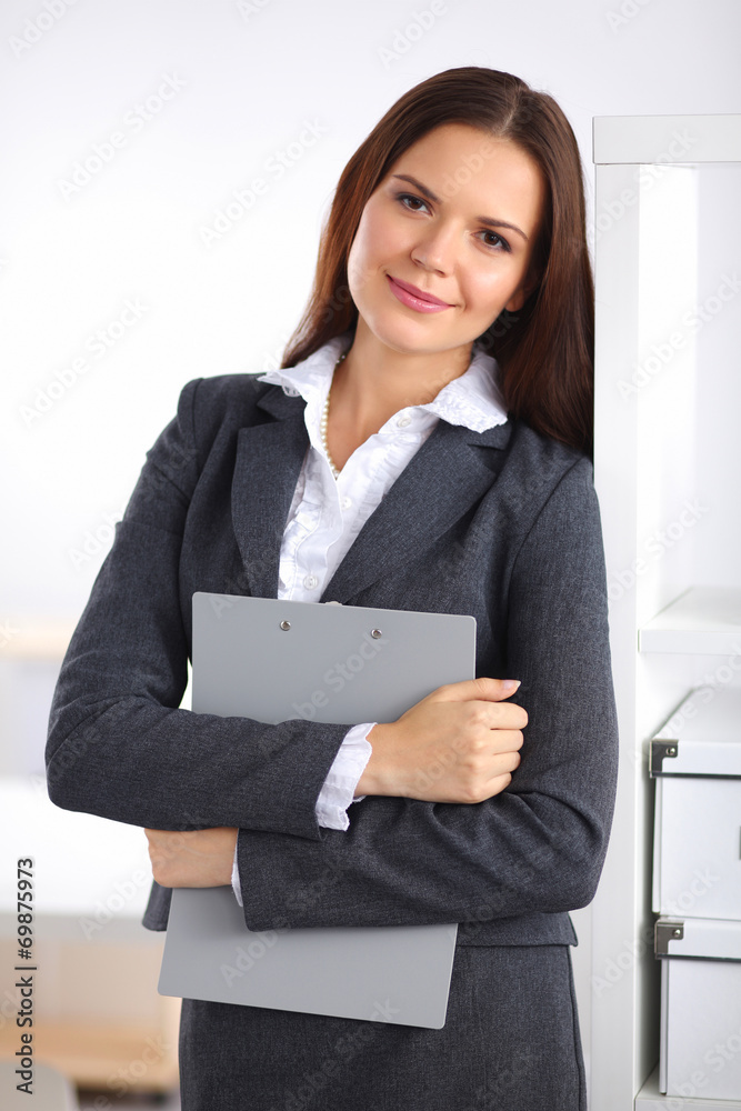 Attractive young businesswoman standing near desk with folder in
