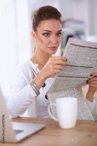 Cute businesswoman holding newspaper sitting at her desk in