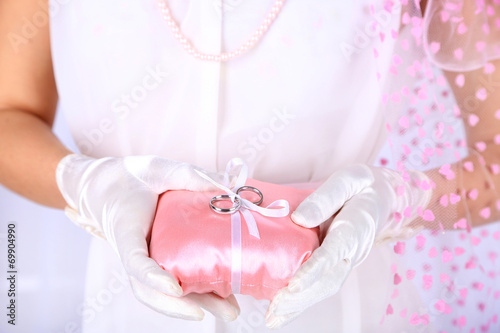 Bride in white dress and gloves holding decorative pillow with