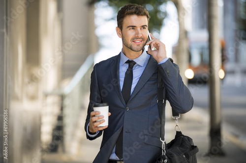 Commuter waiting for the bus with coffee using his cell