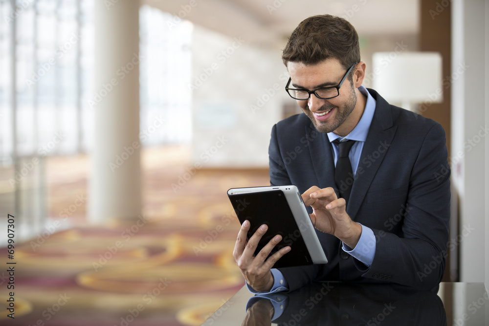 Smiley businessman with glasses using tablet at the hotel lobby