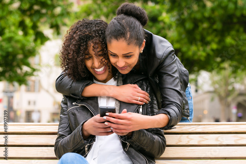 Beste Freunde chatten mit Smartphone auf Parkbank photo