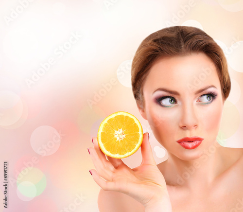 Beautiful young woman with bright make-up, holding orange