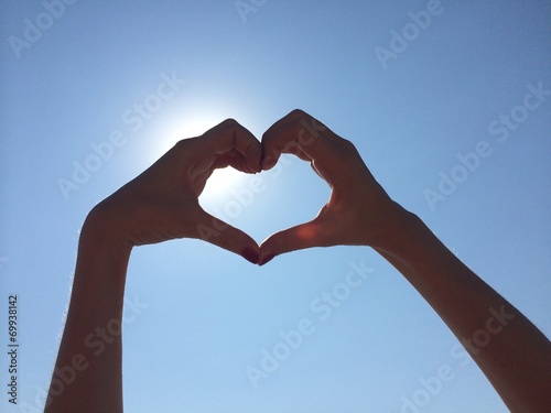 hands show heart shape on sun and blue sky background 