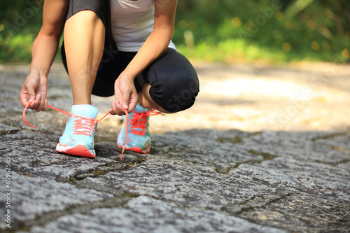 woman runner tying shoelace on stone trail © lzf