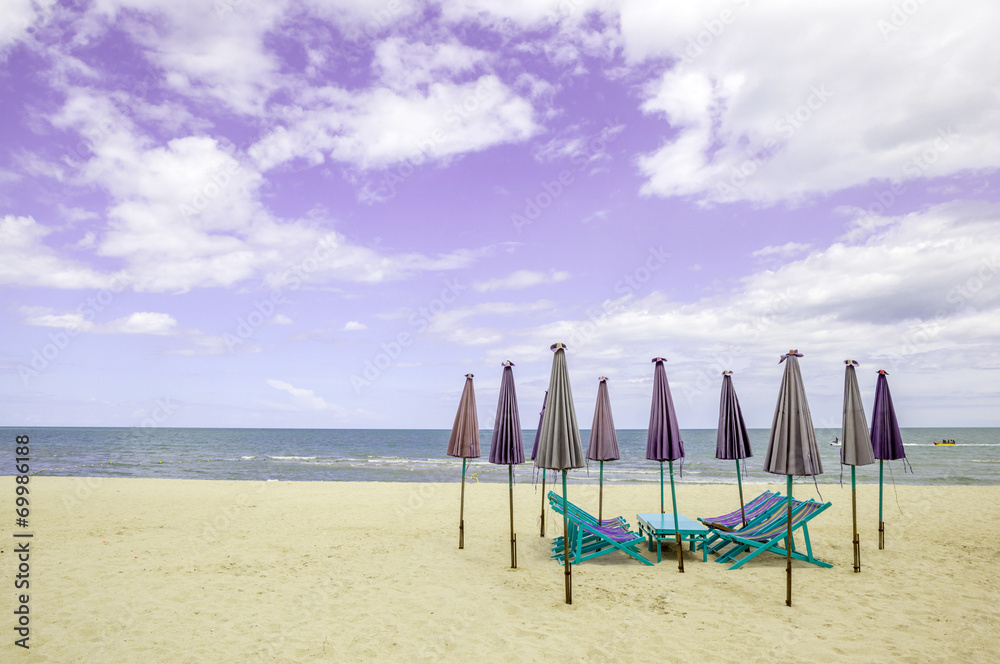 Group of beach chairs and closed umbrellas on white sand beach w Group of beach chairs and closed umbrellas on white sand beach w