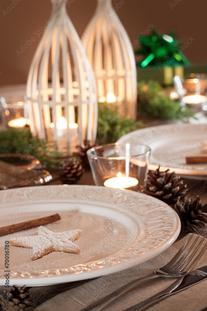 Christmas table setting. Elegant white plates with cookies, natural pine tree branch, pinecones, candles and gifts. Rural or rustic style decorations. Christmas table setting. Elegant white plates with cookies, natural pine tree branch, pinecones, candles and gifts. Rural or rustic style decorations.
