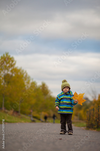 Adorable baby boy playing with yellow leave in autumn park
