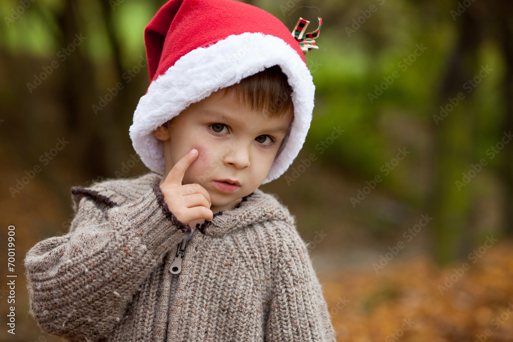 Sad little boy in the park, with santa hat, showing his hurt che Sad little boy in the park, with santa hat, showing his hurt che