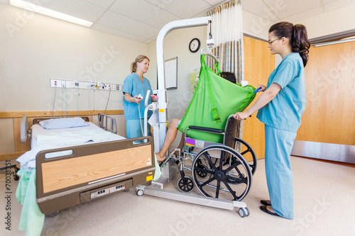 Female Nurses Transferring Patient From Hydraulic Lift To Wheelc photo