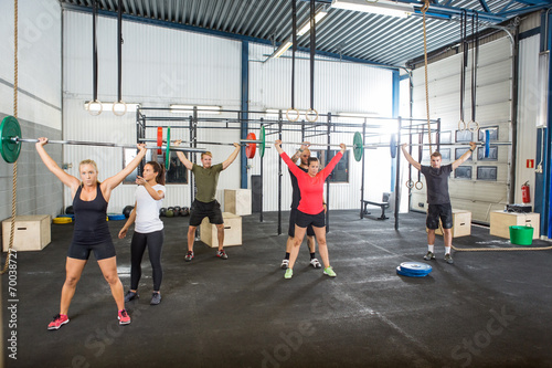 Instructor Assisting Athletes In Lifting Barbells