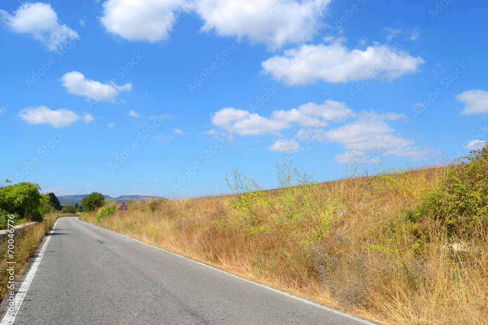 Strada asfaltata con cielo azzurro e nuvole