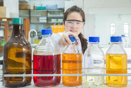 Asian scientist selecting bottle in shelf at laboratory (focus a