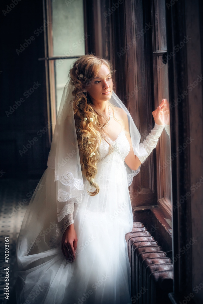 Obraz premium Beautiful bride in white wedding dress standing near the window