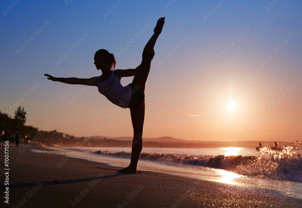 Woman doing a yoga workout at the beach during sunrise
