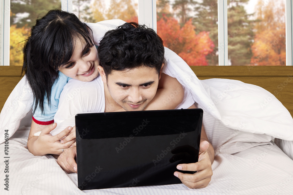 Asian couple using laptop on bed