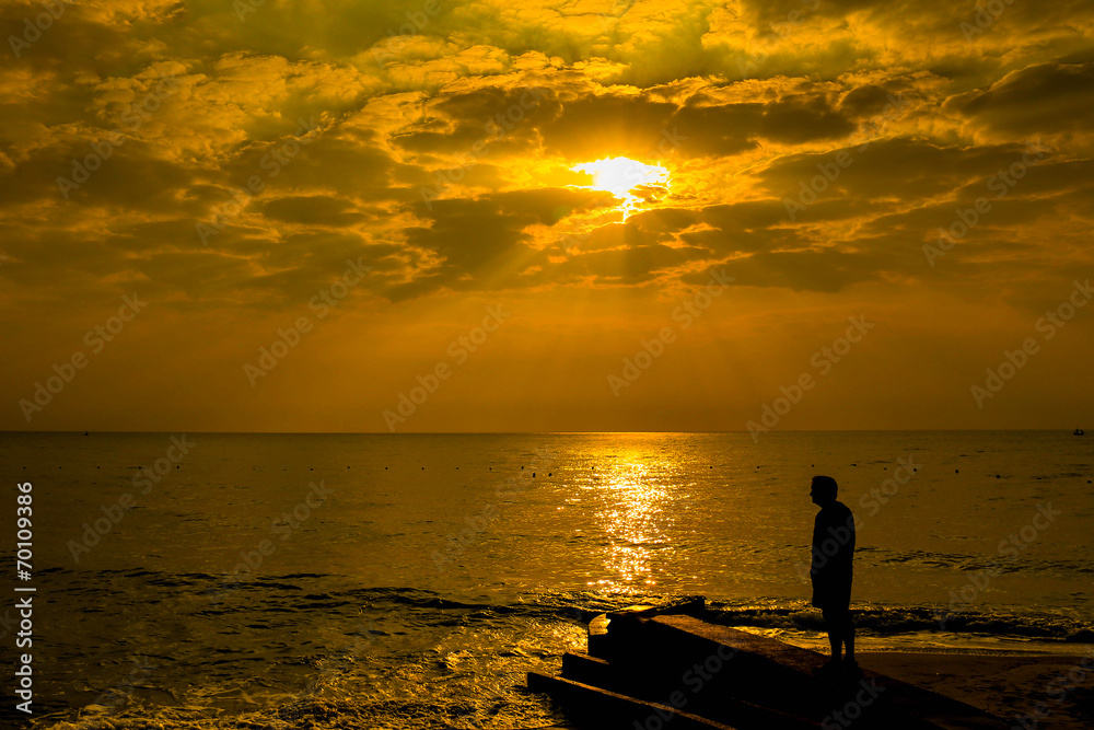 Man standing at the beach looking at bright red storm clouds dur