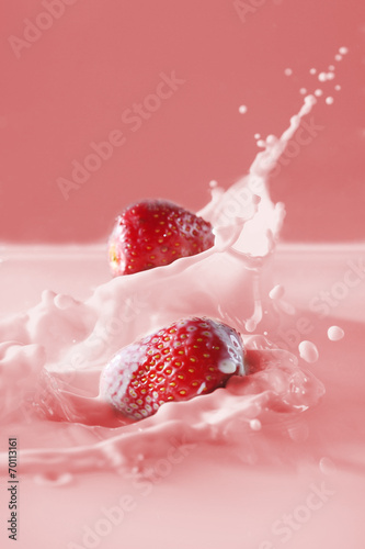 Delicious fresh strawberry falling into splashing milk