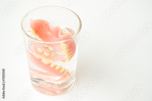 An artificial denture in a glass of water on isolated background