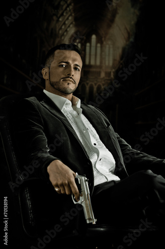 Elegant man sitting in a chair holding  gun over dark background