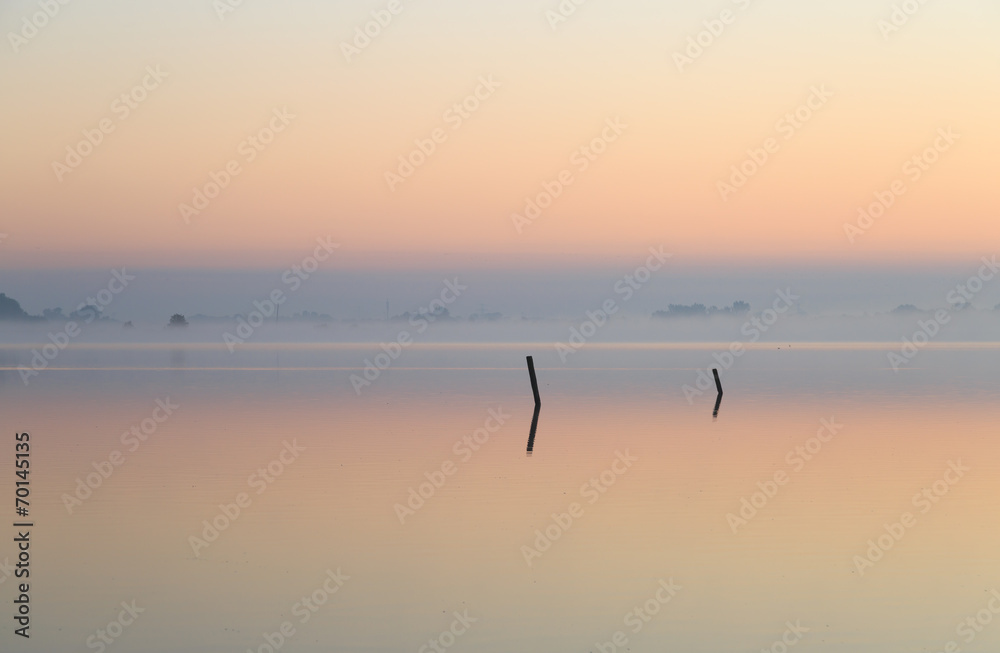 Two poles in a foggy lake at dawn.
