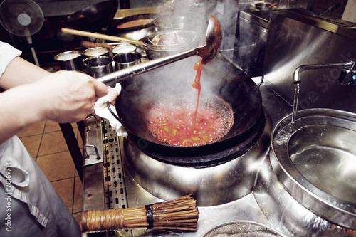 Chef is stirring vegetables with sour sauce in wok photo