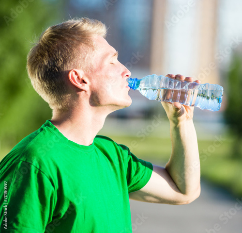 Tired man drinking water from a plastic bottle after fitness