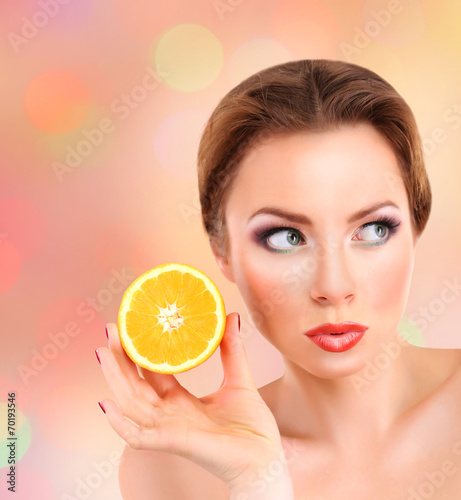 Beautiful young woman with bright make-up, holding orange,