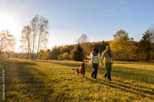 Couple walk dog in countryside autumn sunset