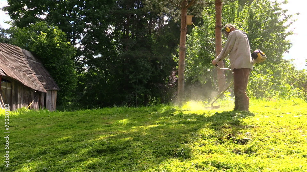 worker trimming green grass with manually petrol lawn trimmer