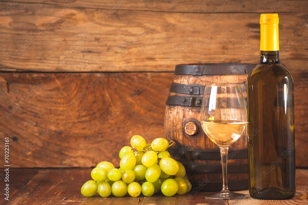 Glass of white wine with bottle and barrel on a rustic wooden ta