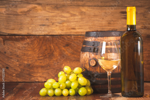 Glass of white wine with bottle and barrel on a rustic wooden ta