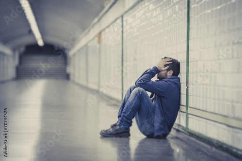 Young sad man sick and depressed sitting on ground street tunnel