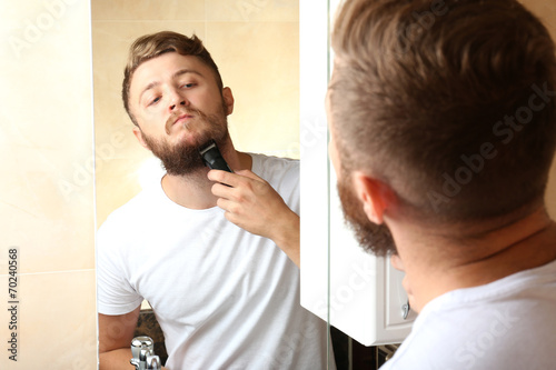 Young man shaving his beard in bathroom