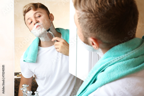 Young man shaving his beard in bathroom