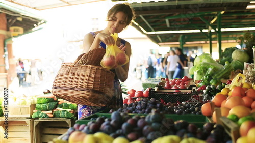 Woman putting tomatoes and peaches to the basket on the market