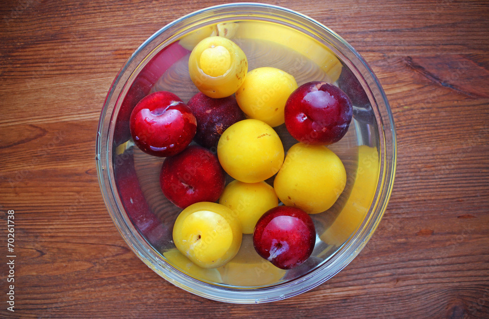 Red and yellow plums in glass dish with water Red and yellow plums in glass dish with water