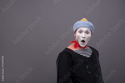 Portrait of young male mime with white face, grey hat showing em