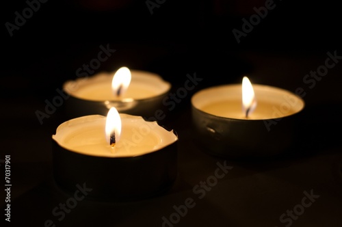 Three burning tea lights on black background. Horizontal image