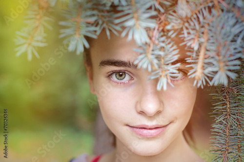 portrait of a smiling girl looking through blurred fir needles