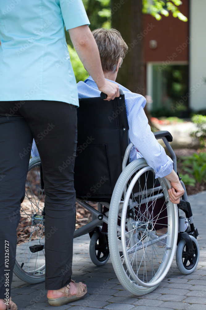 Obraz premium Nurse walking with elderly woman on wheelchair