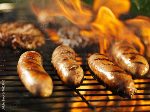 bratwursts cooking on flaming grill photo