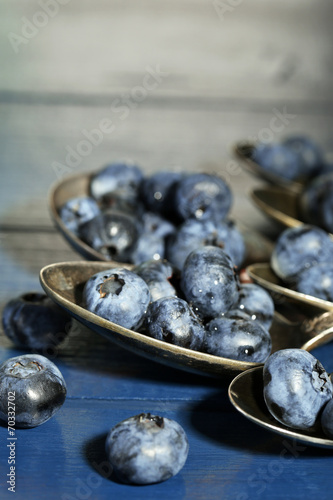 Tasty ripe blueberries in spoons  on wooden background