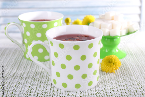 Two cups and sugar on white tablecloth on light background