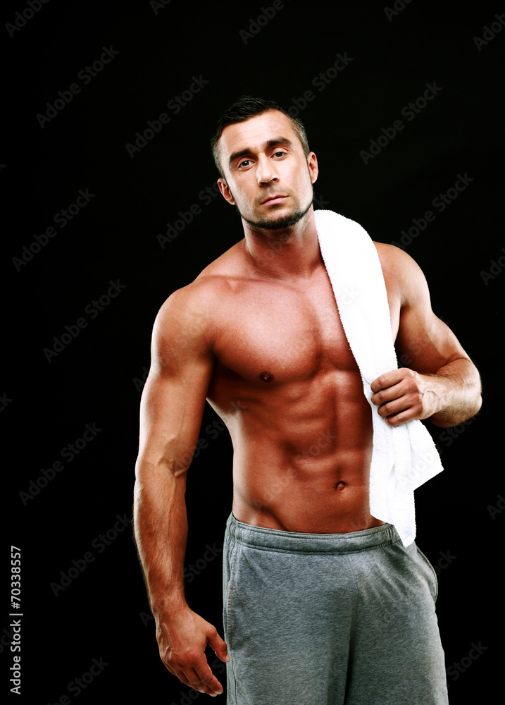 Handsome muscular man holding towel on black background