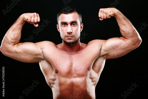 Serious muscular man showing his biceps on black background