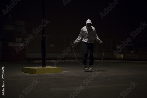 Hooded athlete skipping at night under a street light